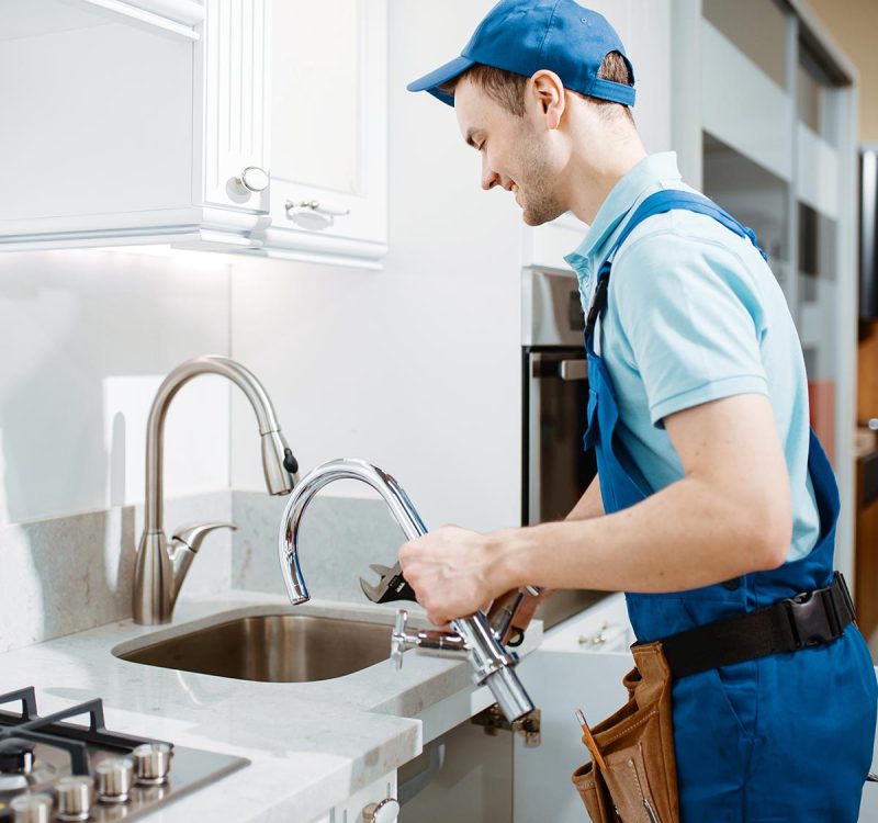 Plumber in uniform changes faucet in the kitchen